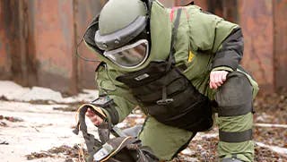 bomb desposal tech in bomb suit analyzing a bomb